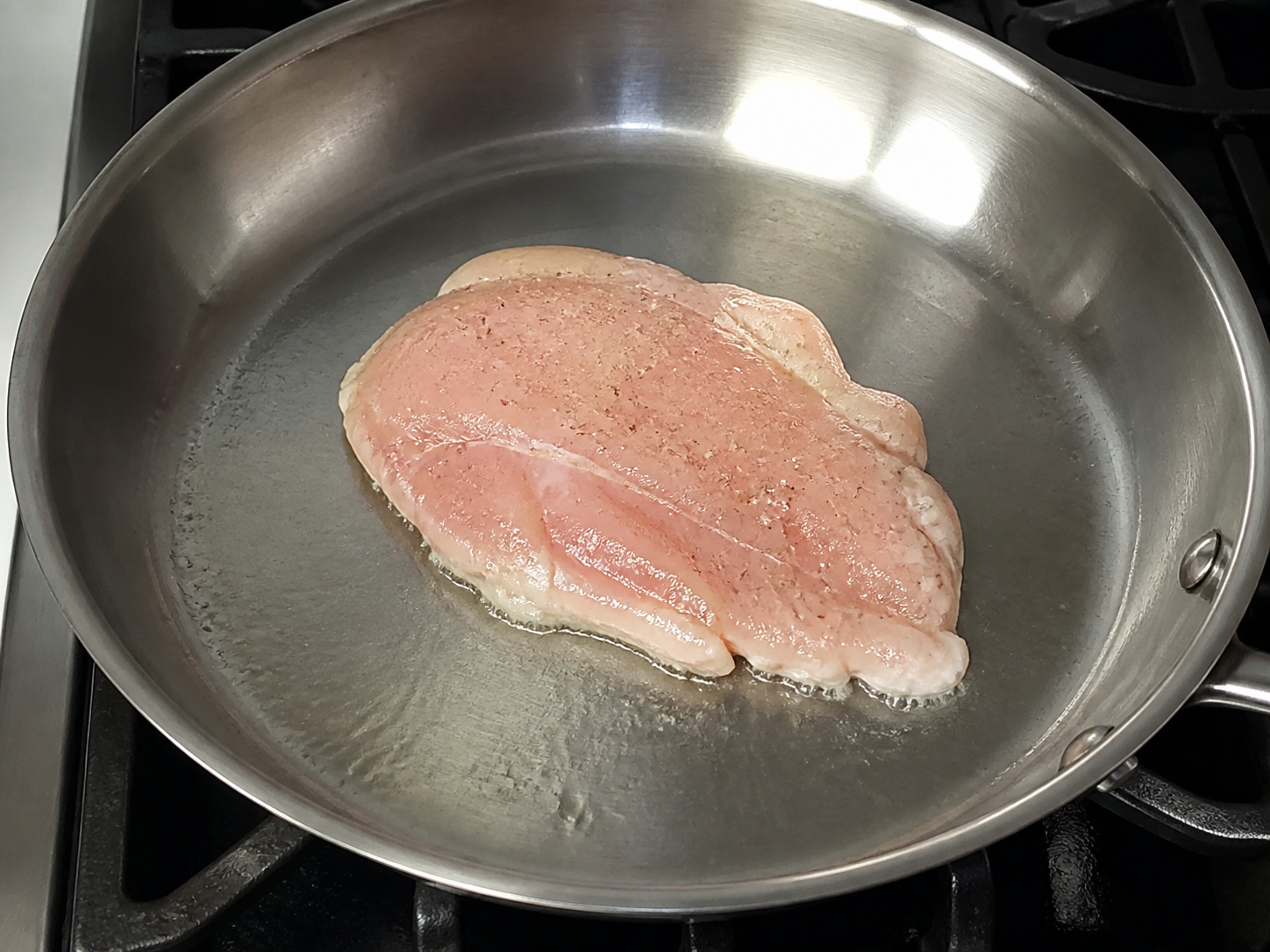 A pale chicken cutlet early in searing before a crust has formed
