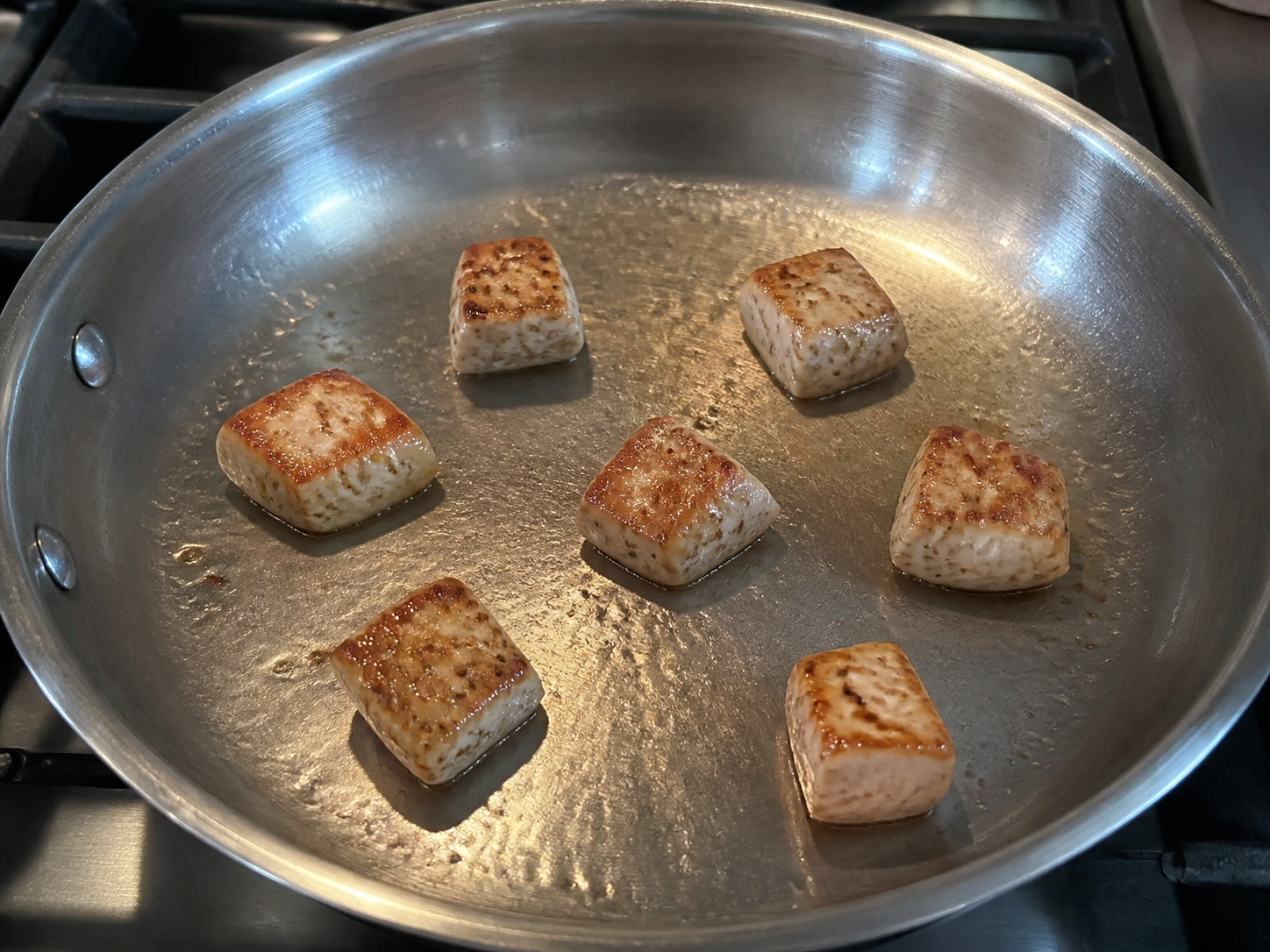 Chicken pieces spaced apart in a skillet and developing a golden crust
